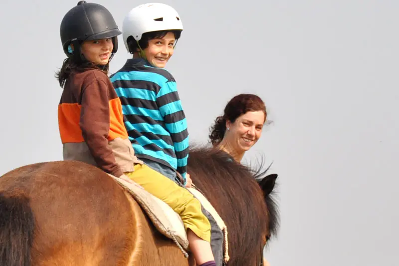 Zwei Kinder gemeinsam auf einem Pferd, begleitet von einer Reitpädagogin