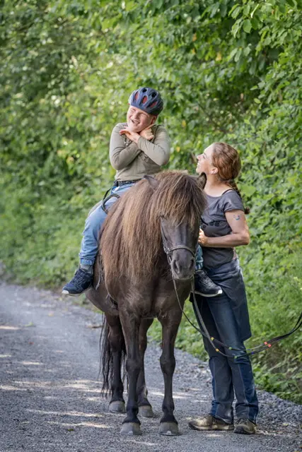 Kind auf einem Pony lacht fröhlich, begleitet zu Fuß
