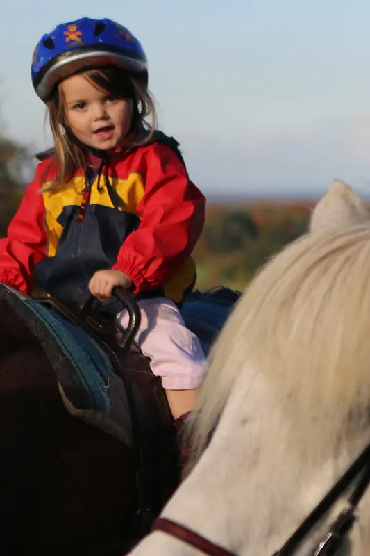 Kind mit Reithelm sitzt im Abendlicht auf einem Pony